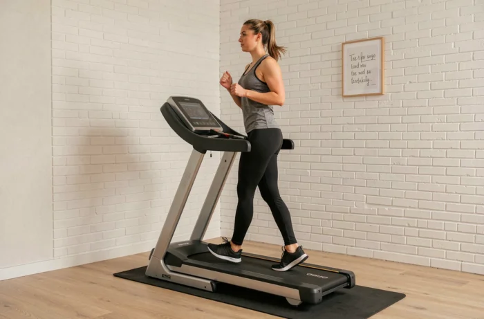 Femme en tenue de sport utilisant le tapis de course Sportstech F10 compact dans un espace fitness maison moderne